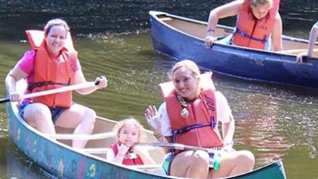 Three girls in a canoe wearing life jackets and smiling